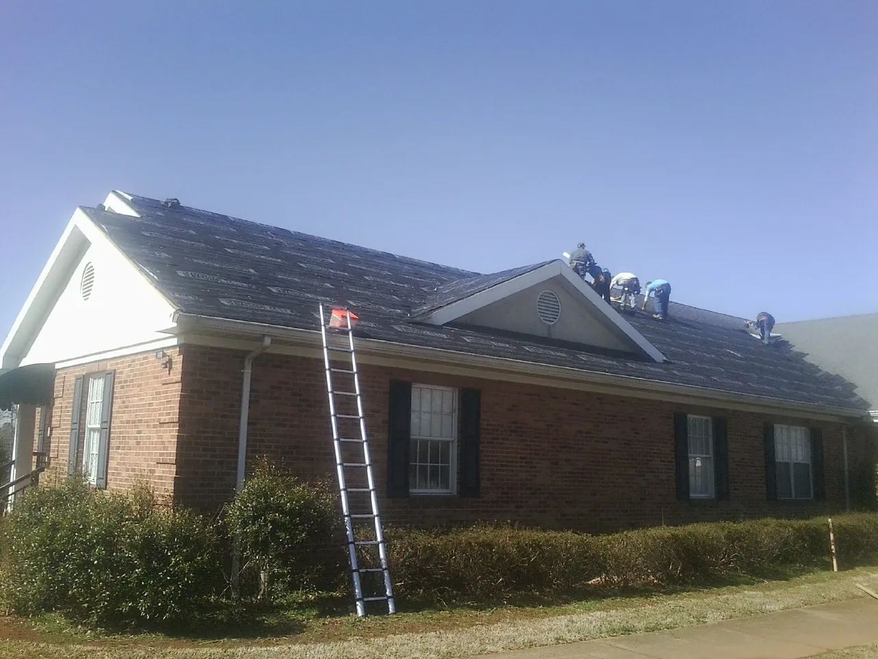 Crew tearing shingles off a brick ranch roof with a ladder set — Metal Roof Repair work by our crew in Dayton