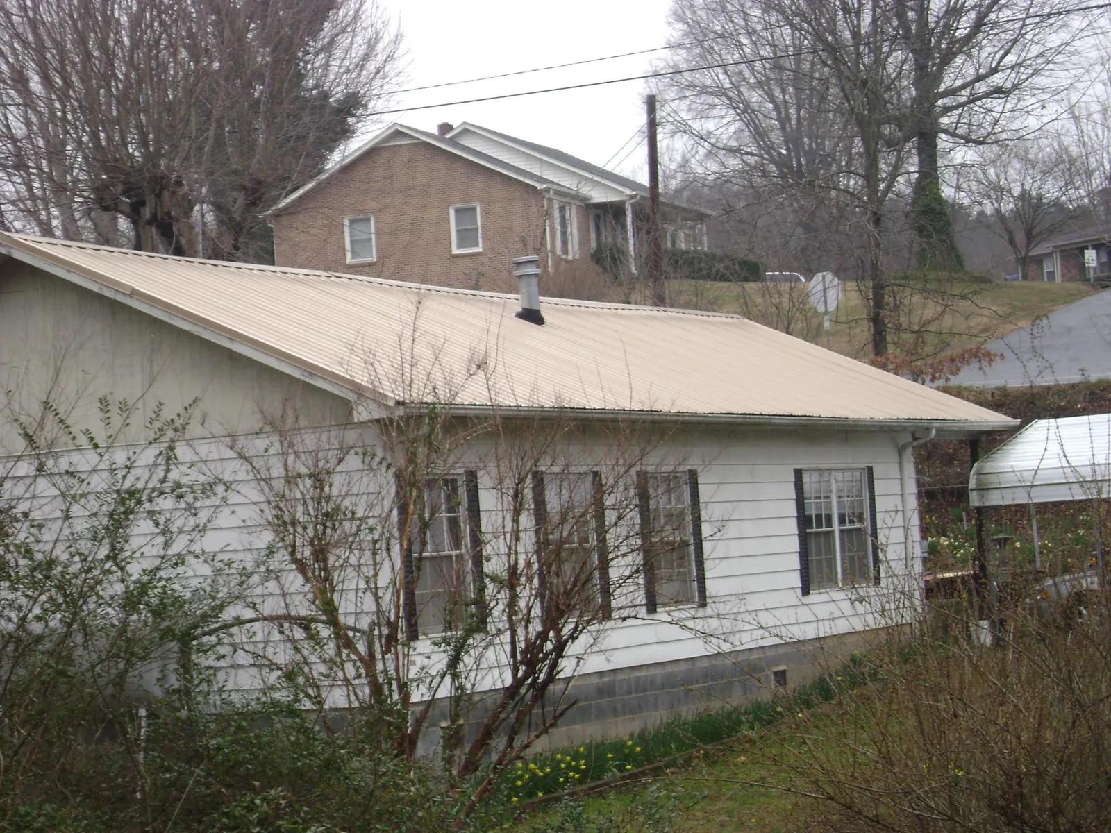 Tan metal roof on a white sided house set into a hillside — Commercial Roofing by Roofing Brothers in Dayton